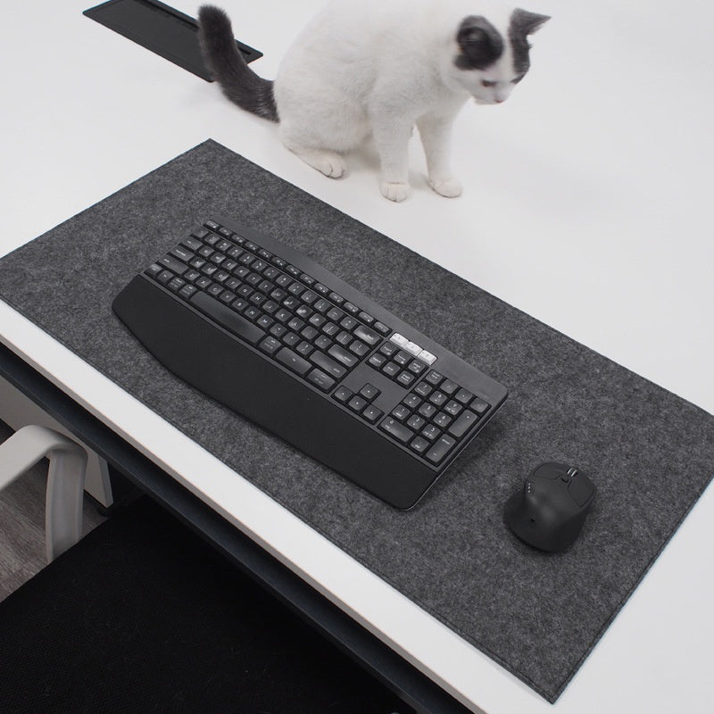 Keyboard on a desk on top of a wool desk pad with a cat sitting nearby