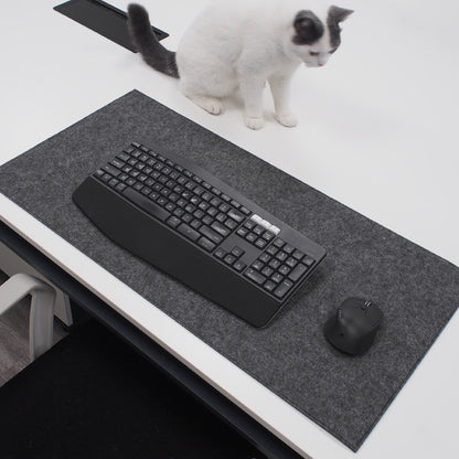 Keyboard on a desk on top of a wool desk pad with a cat sitting nearby